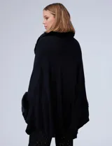 Ruana de tejido color tostado con cuello, bordes frontales y puños amplios con apliques de piel sintética al tono. Presenta una abertura central con cierre de botón tipo trenca.