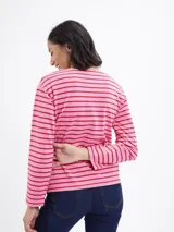 Blusa de manga larga con diseño a rayas horizontales en tonos rosa y rojo. Presenta cuello redondo y detalle de botones decorativos en el lateral inferior.