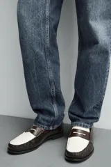 Mocasín de cuero color negro con antifaz en contraste blanco y marrón.