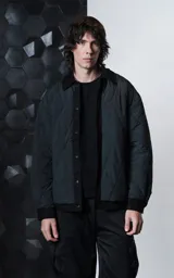 Campera oversize negra confeccionada en microfibra opaca matelaseada con costuras geométricas, cuello, cartera, puños y ruedo de gabardina combinada, cierre frontal con broches a presión y diseño de doble capa en el ruedo.