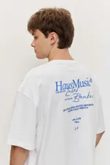 Remera blanca de manga corta, corte oversize, con estampa en la espalda de una flor sobre fondo difuminado verde y blanco.