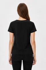 Remera negra de manga corta, con cuello redondo y ajuste al cuerpo. Cuenta con un gran estampado floral en tono gris en el frente y detalle de tachas plateadas alrededor del cuello y en los puños.