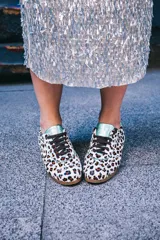 Zapatillas de estilo running con estampado animal print de leopardo sobre fondo blanco. Presentan detalles en piel verde tornasolada en la parte trasera y lengüeta, cordones oscuros y suela de goma dentada con cuña interna.