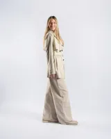 Campera trench de gabardina en color beige, con solapa cruzada, doble botonadura frontal, hombreras y cinturón ajustable para anudar en la cintura. Presenta bolsillos delanteros y puños ajustables con tiras.