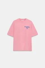 Camiseta oversize de manga corta y cuello redondo, color rosado con efecto lavado, con pequeño texto estampado en azul en el pecho.