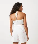 Blusa corta blanca de algodón con bordado de palmeras color naranja, escote halter y espalda descubierta.