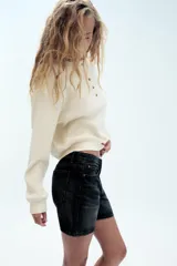 Bermuda de tiro medio confeccionada en denim de color negro gastado, con diseño de cinco bolsillos, trabillas para cinturón y cierre frontal con cremallera y botón metálico.