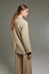 Blazer color beige de lana, con calce recto, solapas de muesca, cierre frontal con dos botones metálicos personalizados, bolsillos con solapa y bordado dorado en la manga.