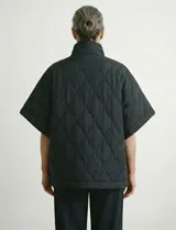 Poncho acolchado color vino tinto, con cuello alto y cierre frontal parcial. Presenta un patrón de costuras capitoné en forma de hoja o diamante y bolsillos delanteros.