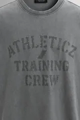 Camiseta de corte regular fit confeccionada en algodón, con cuello redondo y manga corta. Presenta un estampado frontal con el texto 'ATHLETICZ TRAINING CREW' con efecto desgastado.
