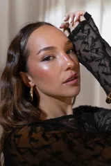 Vestido corto negro de encaje transparente, con mangas largas y falda ajustada con detalle lateral asimétrico tipo pareo.