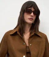 Chaqueta de corte recto confeccionada en suede sintético color marrón. Presenta cuello estilo camisa, cierre frontal con botones metálicos, mangas largas con puños ajustados y bolsillos embutidos.