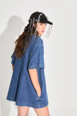 Vestido corto de denim azul con corte holgado, mangas cortas y bolsillo frontal con logo bordado. Cuenta con cierre metálico en la espalda.