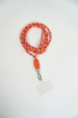 Correa para celular de cuerda trenzada en tonos naranja y fucsia, con detalle de cuero sintético naranja y gancho metálico tipo mosquetón que incluye una placa transparente para sujeción.