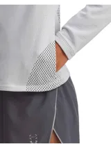 Buzo deportivo gris claro para mujer, con cierre frontal completo, cuello alto y mangas largas. Presenta paneles de malla calada en hombros, mangas y espalda para mayor transpirabilidad. Logo de la marca en el cuello.