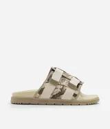 Ojota tipo slide con estampa camuflada en tonos beige y marrón. Presenta dos tiras ajustables con cierre de velcro y suela de goma antideslizante.