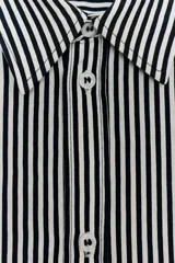 Camisa de corte fluido confeccionada en mezcla de viscosa, con diseño de rayas verticales en blanco y negro. Presenta cuello solapa, manga larga con puños, bolsillo de plastrón en el pecho, bajo redondeado y cierre frontal con botones.