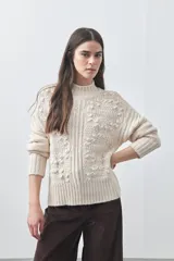 Polera de tejido de punto color crudo con cuello alto y diseño tramado con relieve de pompones. Presenta puños y ruedo acanalados, con un calce holgado y cómodo.
