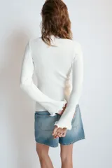 Chaqueta de punto rib color blanco, con cuello redondo, manga larga con acabado ondulado en los puños y cierre frontal con botones.