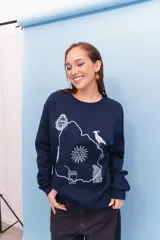 Buzo de cuello redondo en color blanco, con diseño estampado en el centro que incluye el contorno del mapa de Uruguay y símbolos nacionales como el sol, el mate y el hornero.