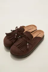 Suecos tipo mocasín color chocolate, confeccionados en material gamuzado. Presentan un diseño con flecos frontales, cordones decorativos con cuentas y una suela de plataforma plana de goma.