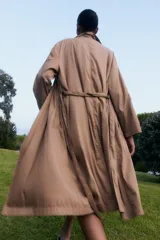 Trench coat color beige de corte largo, confeccionado en lyocell, con cuello solapa y cinturón ajustable del mismo material.