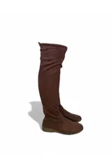 Bota bucanera de gamuza marrón, de caña alta elástica por encima de la rodilla, punta redondeada, suela plana y cierre lateral interno.