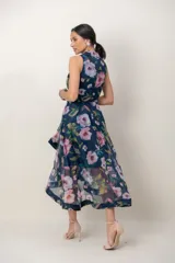 Vestido midi de organza azul marino con estampa floral en tonos rosados y verdes. Presenta escote en V cruzado con solapas, sin mangas, falda evasé de capas asimétricas y estructuradas.