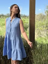 Vestido celeste de lino, sin mangas, con cuello mao y botones de nácar. Presenta varios cortes en su largo, aportando movimiento y un toque moderno a este diseño fresco y elegante.