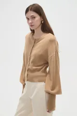 Saco de punto color beige, con cuello redondo, cierre frontal con botones y mangas largas con puños acanalados.