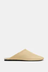 Zapato tipo mule de mujer confeccionado en piel con textura de pelo en color beige. Presenta un diseño de punta redonda y suela plana en contraste.