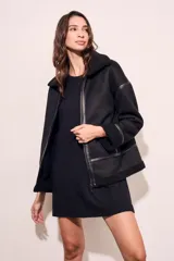 Campera tipo gamulán de corte oversize, color negro, con interior y cuello de corderito sintético. Presenta cierre frontal, detalles de costuras y puños con terminación en corderito.