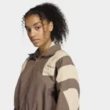Campera deportiva Adidas de corte holgado, con cierre frontal y cuello alto. Presenta un diseño en bloques de color marrón y beige, con detalles inspirados en la estética futbolística de los años 90.