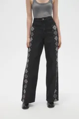 Pantalon de jean negro de corte ancho y tiro alto, con estampado de rombos en los laterales de las piernas.