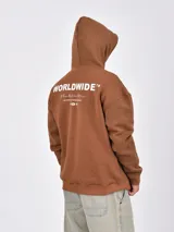 Canguro de tejido grueso color marrón, con capucha y bolsillo canguro frontal. Presenta un estampado minimalista en el pecho con texto y un diseño abstracto.