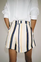 Shorts de tiro medio con trabillas en la cintura y cierre frontal con cremallera y botón. Presenta pliegues delanteros y bolsillos laterales ocultos en la costura, con un diseño de rayas verticales multicolor.