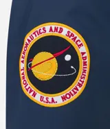 Campera rompevientos azul marino con capucha, cierre frontal y bolsillos laterales. Presenta estampado de NASA en el pecho, parche de bandera estadounidense en la manga y bolsillo utilitario en el brazo.