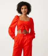 Blusa cropped roja de lino y viscosa, con escote cuadrado, mangas largas abullonadas y lazo frontal.