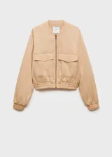 Chaqueta tipo bomber color beige, con cierre frontal de cremallera, cuello redondo, bolsillos de solapa en el pecho y cintura y puños elásticos.