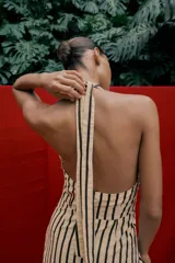 Vestido midi de corte globo con estampado de rayas verticales, cuello halter anudado, escote en pico y espalda descubierta. Presenta bajo abullonado con elástico interior y cierre lateral con cremallera oculta.