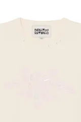 Camiseta cropped de corte relajado, color beige, con cuello redondo y mangas cortas. Cuenta con un estampado frontal con texto en tonos rosados y detalles de efecto desgastado en el cuello.
