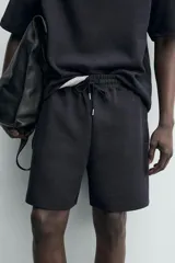 Bermuda estilo jogger de ajuste relajado, color negro, confeccionada en tejido interlock de algodón. Cuenta con cintura elástica ajustable mediante cordón, bolsillos delanteros tipo vivo y diseño liso.