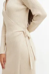 Vestido midi color crema, tejido en punto acanalado, con escote cruzado en V, mangas largas y lazo ajustable en la cintura.