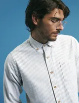 Camisa de manga larga con estampado de rayas verticales finas en tonos gris y blanco. Presenta cuello button-down, bolsillo frontal en el pecho y botones de madera.