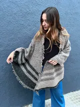 Ruana de lana con diseño a rayas en tonos gris y negro, con detalles de lurex brillante y terminaciones de flecos en los bordes.