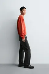 Sudadera de corte relajado, color naranja con efecto tie-dye/deslavado, cuello redondo y manga larga. Presenta un estampado frontal con texto y un trébol de cuatro hojas en amarillo.