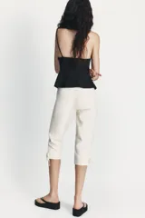 Pantalón capri de tiro alto en color crudo, con detalle de lazos ajustables en los bajos y cierre lateral con cremallera oculta.