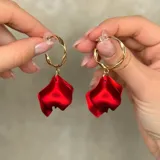 Aros de tipo argolla dorada con diseño retorcido, de los cuales cuelga un dije en forma de pétalo de flor en color rojo vibrante.