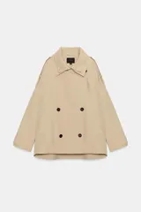 Trench corto oversize color beige con cuello subido de efecto doble, cierre cruzado con botones oscuros y bolsillos de vivo delanteros.