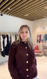 Cardigan de punto trenzado color beige, con cuello redondo, cierre frontal con botones dorados y mangas largas con puños acanalados.